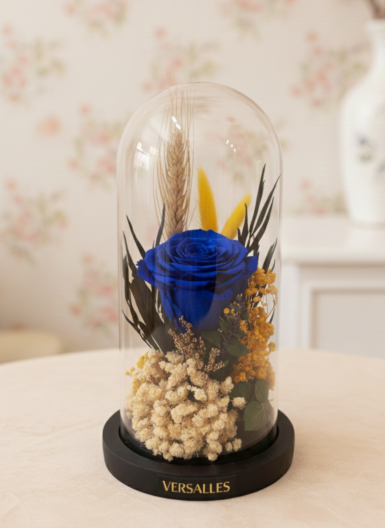 Decorative display with a blue rose and dried flowers under a glass dome, branded 'Versalles'.