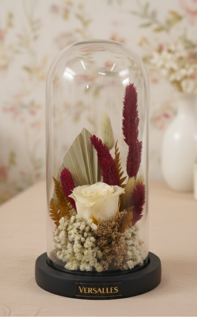 Decorative glass dome with preserved flowers and Versailles branding on a wooden surface.