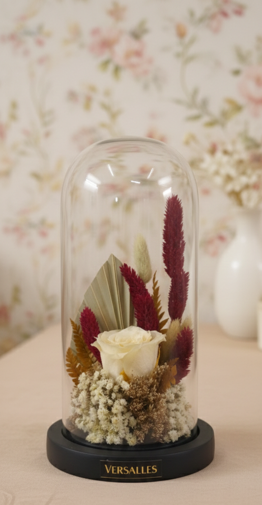 Decorative glass dome with preserved flowers and Versailles branding on a wooden surface.